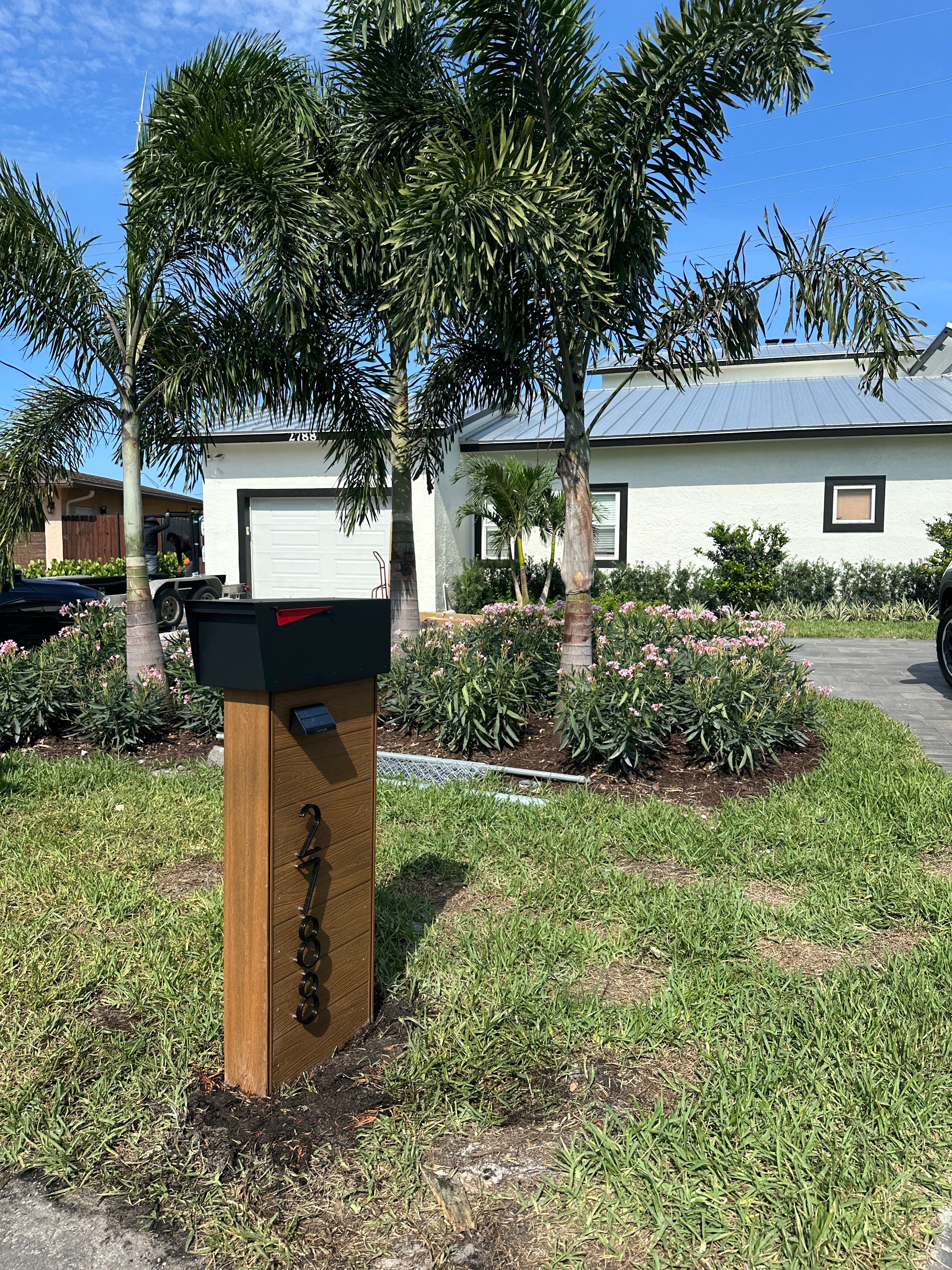 Wooden mailbox on a grassy lawn with palm trees and a house in the background